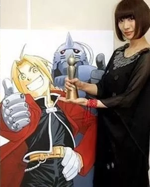 L'autrice Arakawa Hiromu à coté d'une affiche de son manga phare Fullmetal Alchemist
